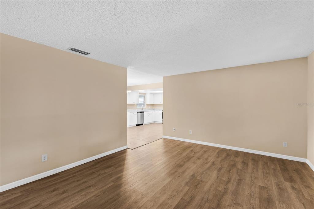 An empty room with light-colored walls and wood-look flooring leads into a white kitchen — 113 LIDO ROAD, WINTER SPRINGS, FL