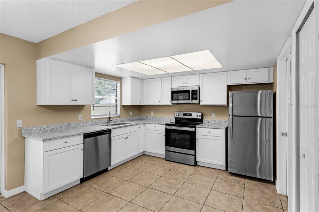 A kitchen features white cabinets, granite countertops, stainless steel appliances, and light-colored tile flooring — 113 LIDO ROAD, WINTER SPRINGS, FL