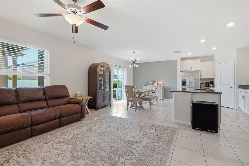 An open-concept living and dining area features a brown leather sofa, tile flooring, and kitchen — 14471 ENGLISH LAVENDER DRIVE, WIMAUMA, FL