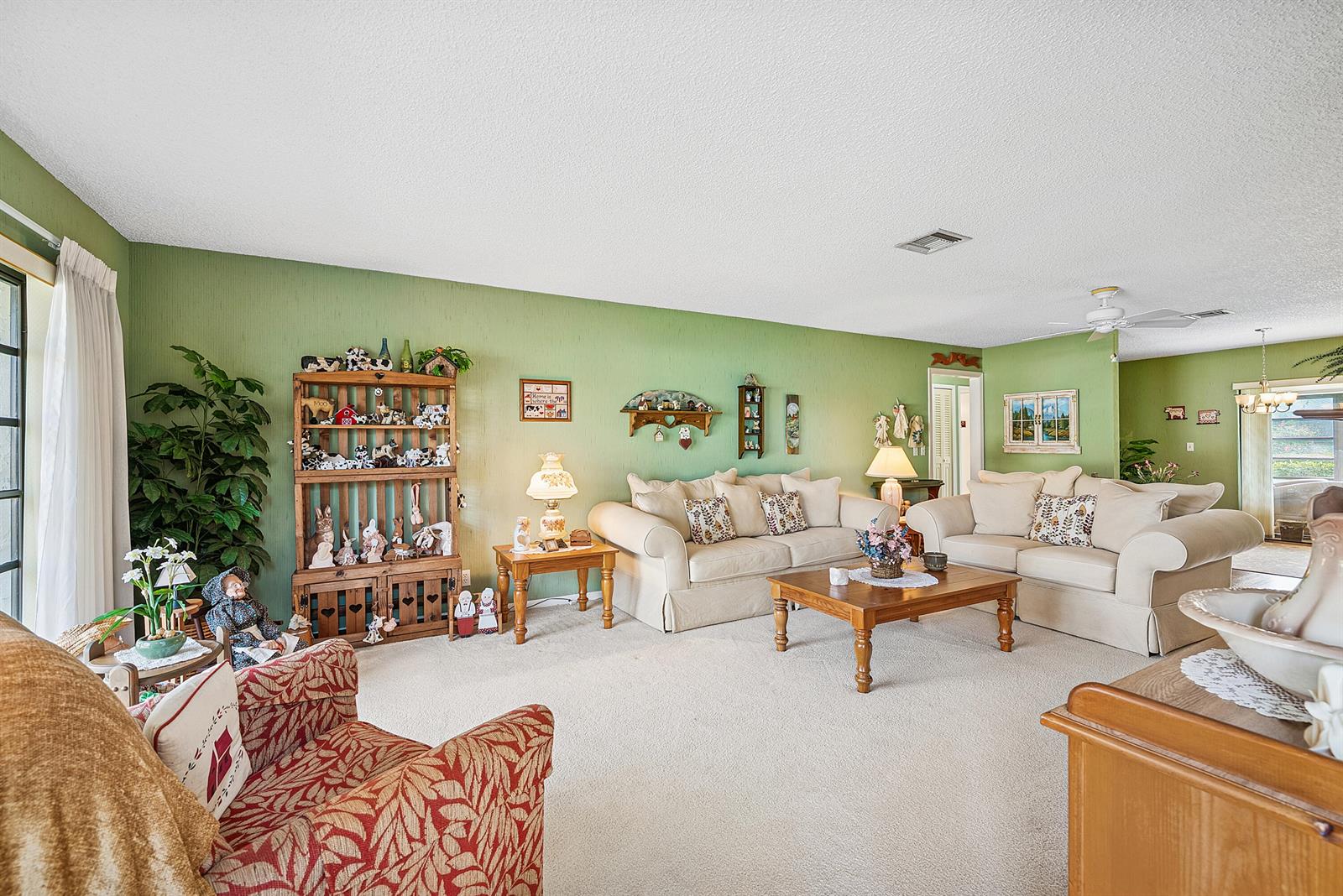 A living room features green walls, beige sofas, a patterned armchair, and a wooden shelf — 4866 Equestrian Road # A, Boynton Beach FL 33436, BOYNTON BEACH, FL