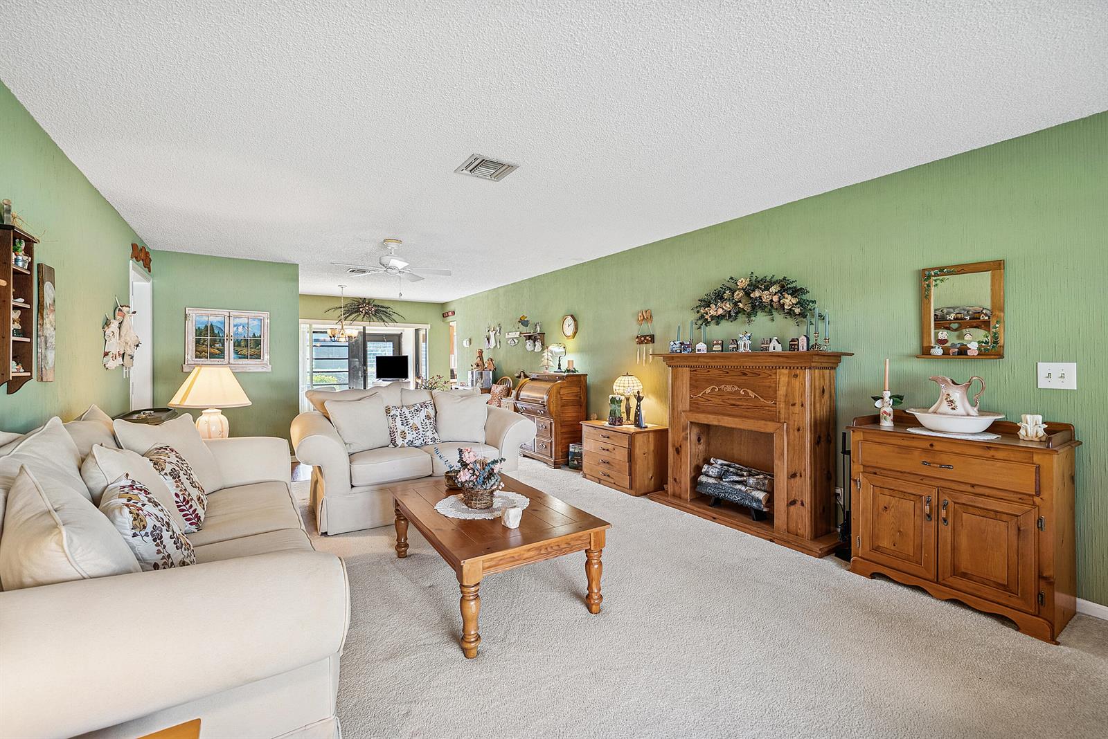 A living room features green textured walls, a wooden fireplace, and light-colored sofas — 4866 Equestrian Road # A, Boynton Beach FL 33436, BOYNTON BEACH, FL