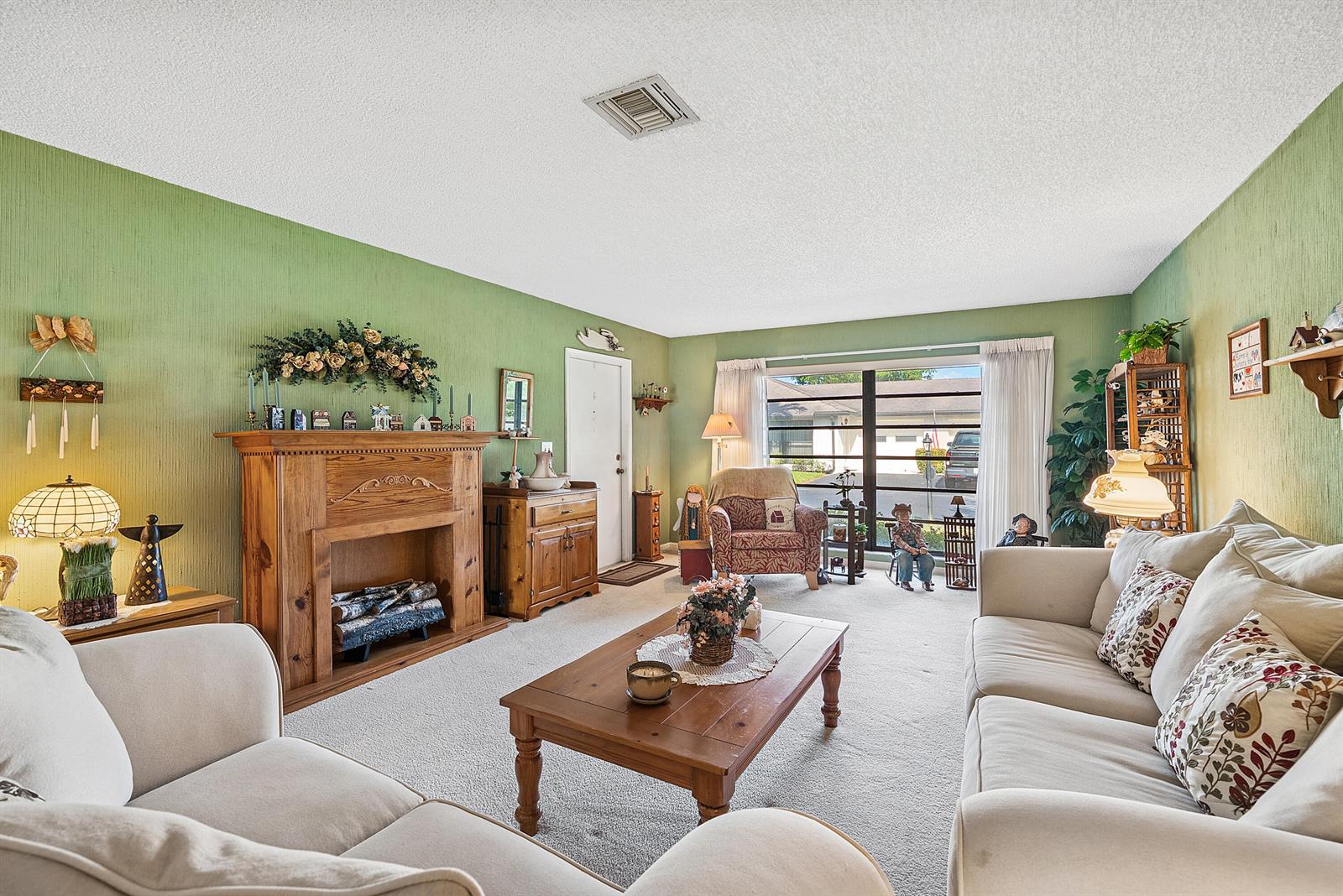 A living room features green textured walls, a wooden fireplace, and beige upholstered furniture — 4866 Equestrian Road # A, Boynton Beach FL 33436, BOYNTON BEACH, FL