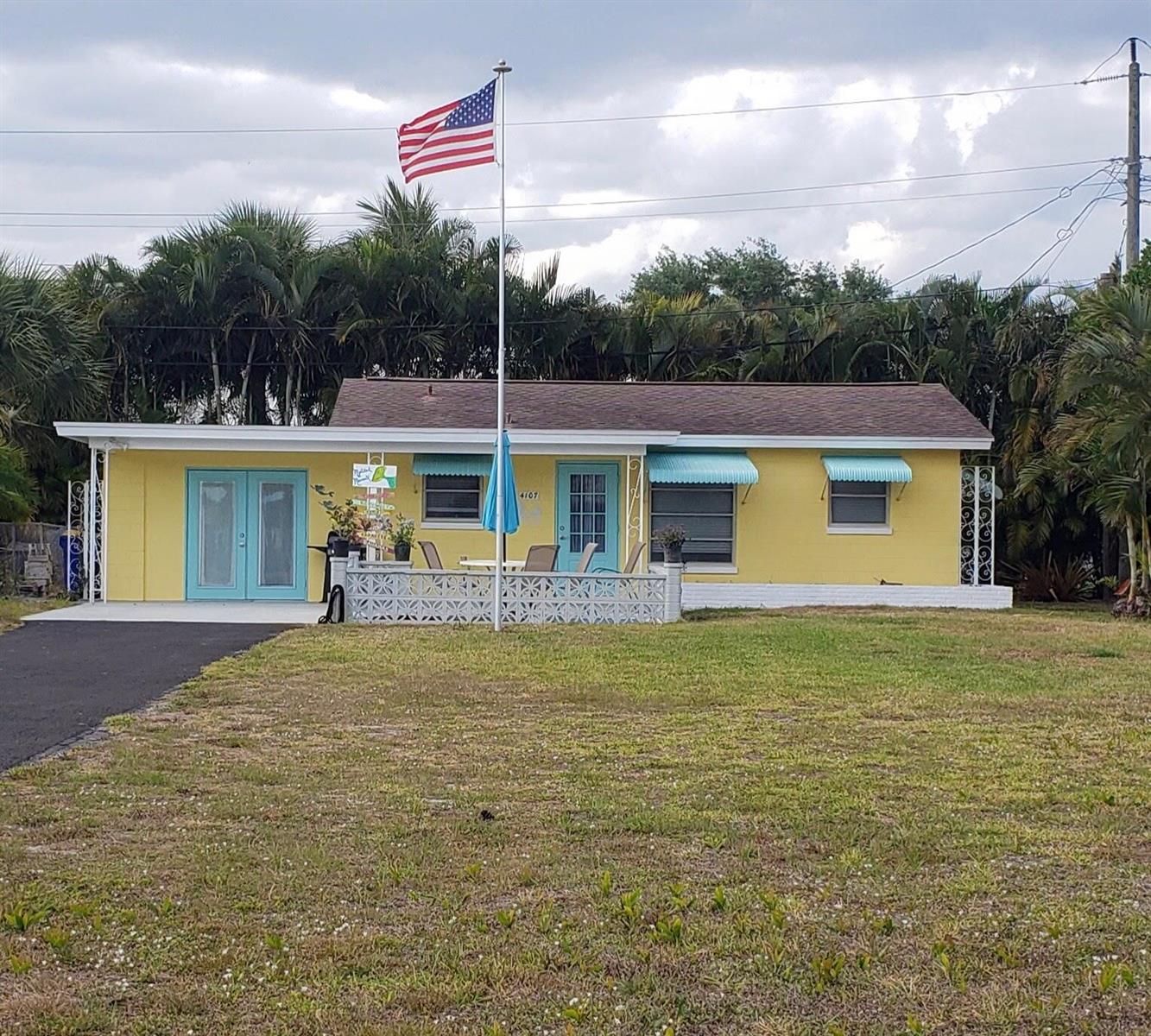 A yellow single-story house with a front patio, turquoise doors, and an American flag — 4107 SE Barcelona Street, Stuart FL 34997, STUART, FL