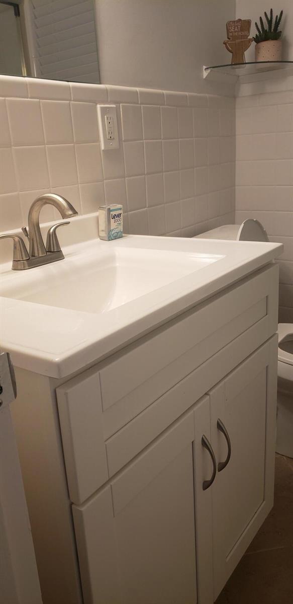 A bathroom features a white vanity with a sink, a tiled backsplash, and a mirror — 4107 SE Barcelona Street, Stuart FL 34997, STUART, FL