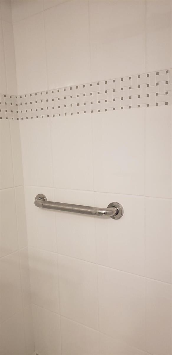 A chrome grab bar is mounted on a white tiled shower wall with a decorative border — 4107 SE Barcelona Street, Stuart FL 34997, STUART, FL