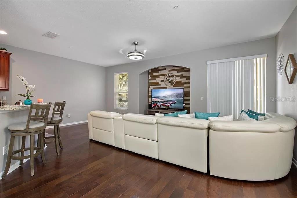 A living room features a white sectional sofa, wood flooring, and a wood-paneled media wall — 1131 LITTLE GEM LOOP, SANFORD, FL