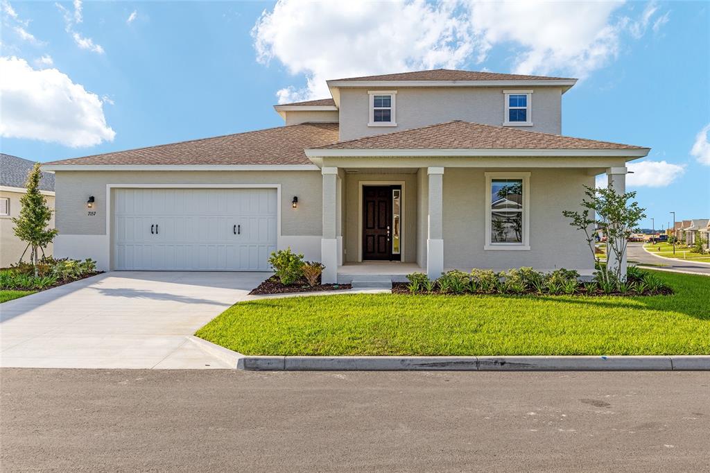 A two-story suburban house with a two-car garage, tan stucco siding, and a shingled roof — 7157 SW 57TH PLACE, OCALA, FL