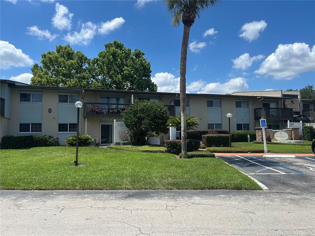 A two-story apartment building features beige siding, balconies, and a palm tree in the front — 1695 LEE ROAD UNIT A103, WINTER PARK, FL