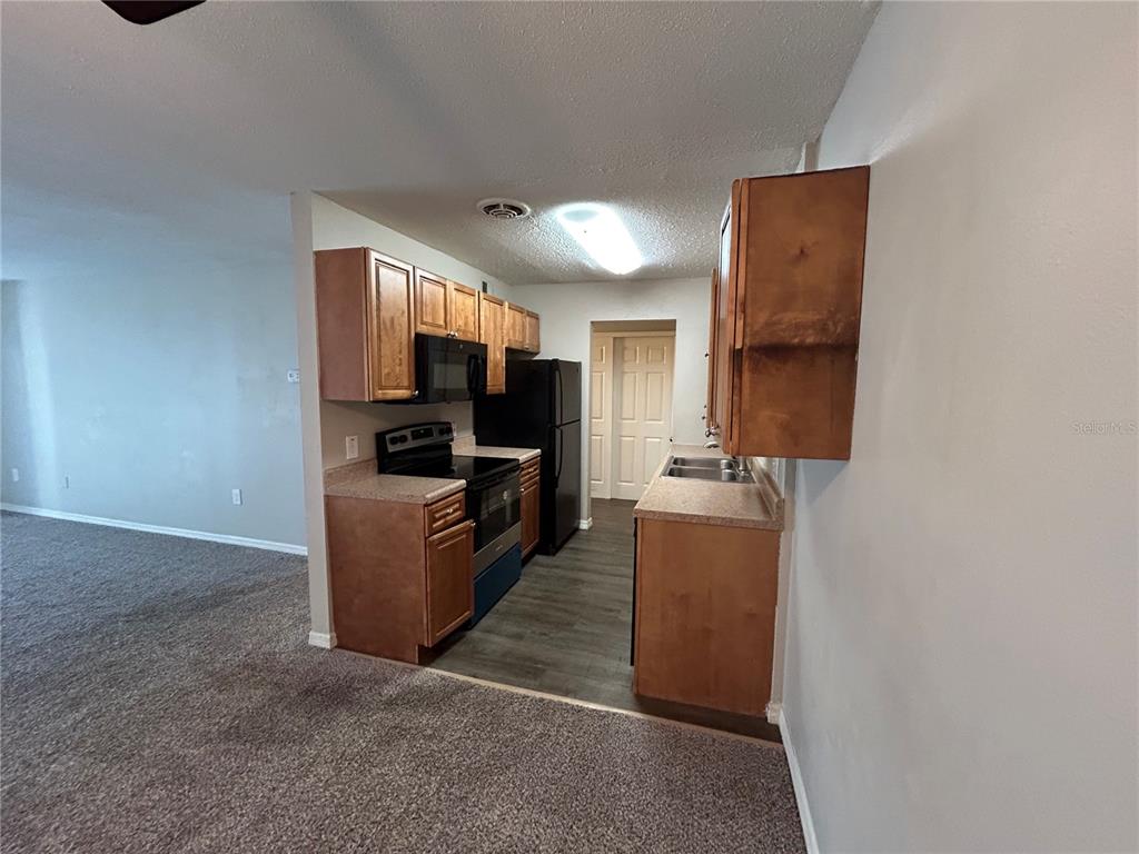 A galley kitchen features wood cabinets, black appliances, and laminate countertops — 1695 LEE ROAD UNIT A103, WINTER PARK, FL