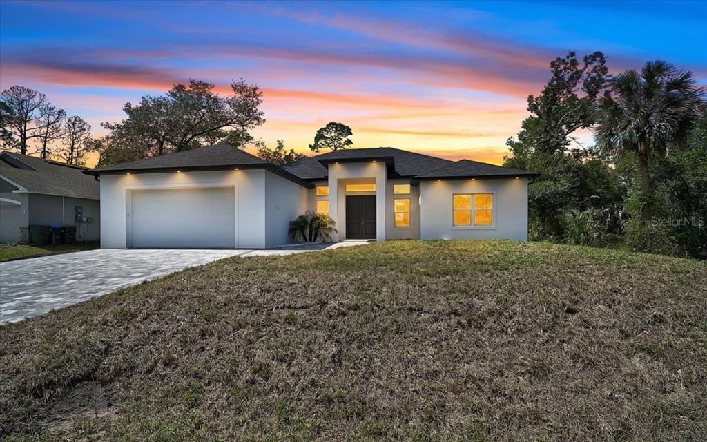 A modern single-story house with a two-car garage and a paved driveway at sunset — 4443 WINDSONG AVENUE, NORTH PORT, FL