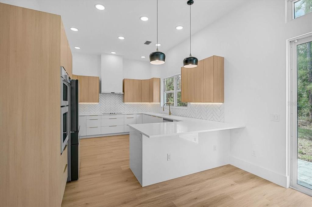 A modern kitchen features light wood cabinets, white countertops, a herringbone backsplash, and two pendant lights — 4443 WINDSONG AVENUE, NORTH PORT, FL