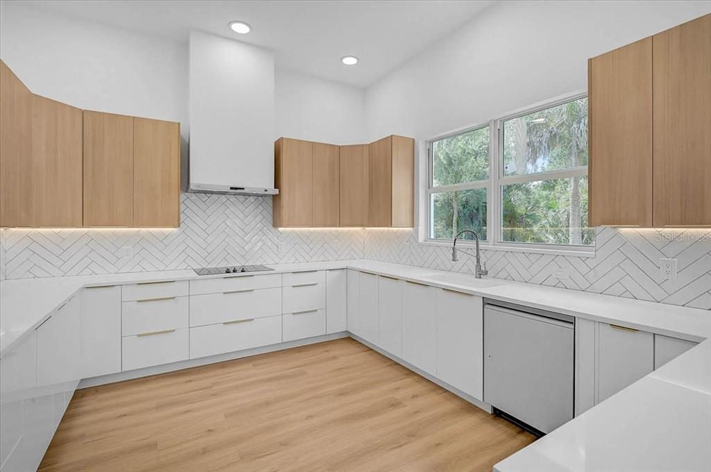 A modern kitchen features white lower cabinets, light wood upper cabinets, and a herringbone backsplash — 4443 WINDSONG AVENUE, NORTH PORT, FL
