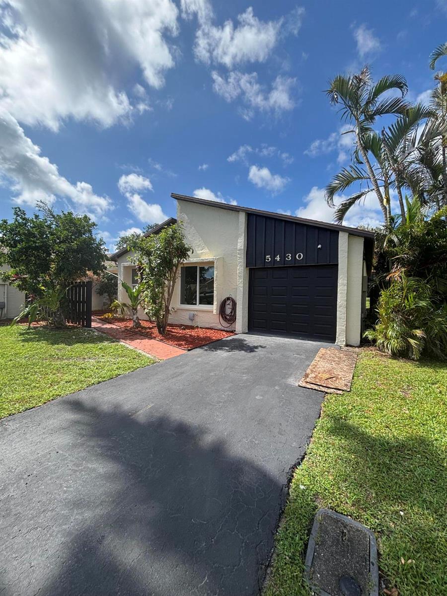 A single-story house with a black garage door, white stucco walls, and a brick walkway — 5430 Mirror Lakes Boulevard, Boynton Beach FL 33472, BOYNTON BEACH, FL