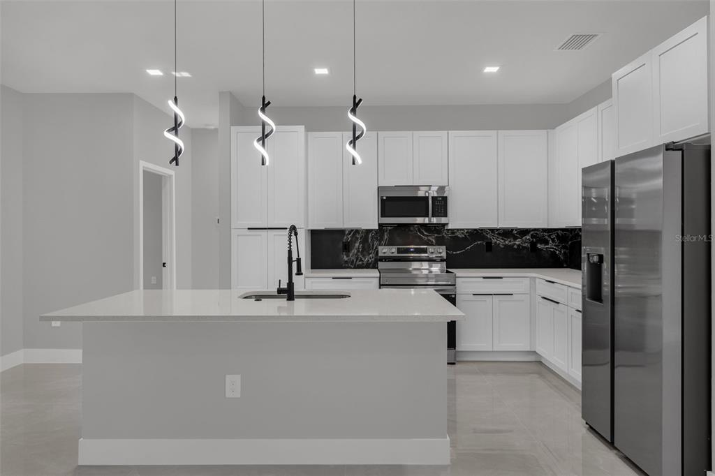A modern kitchen features white cabinets, a black marble backsplash, and a central island — 7753 SW 131 ST LANE, OCALA, FL