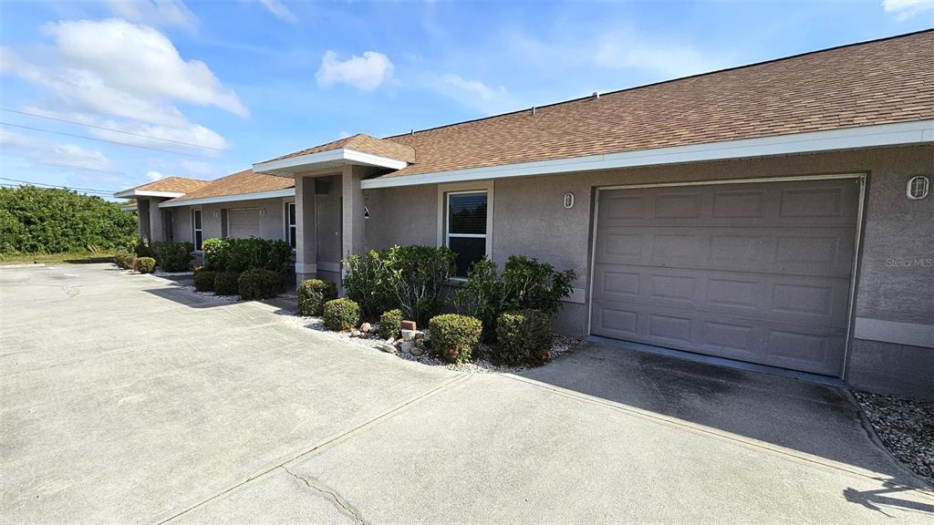 A single-story building with a tan stucco exterior, a brown shingled roof, and garage doors — 309 BOUNDARY BOULEVARD UNIT B, ROTONDA WEST, FL