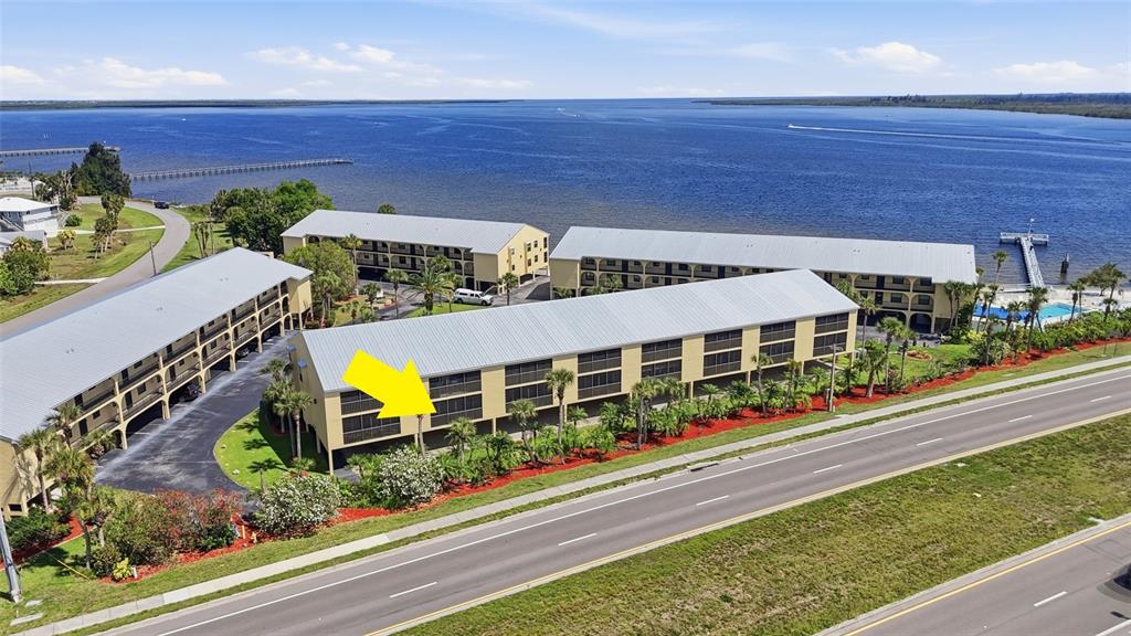 An aerial view shows multi-story apartment buildings with metal roofs located along a waterfront — 14459 RIVER BEACH DRIVE UNIT 115, PORT CHARLOTTE, FL