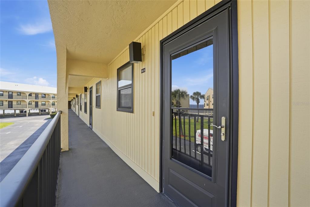 An exterior walkway with yellow siding, a dark door, and a metal railing — 14459 RIVER BEACH DRIVE UNIT 115, PORT CHARLOTTE, FL
