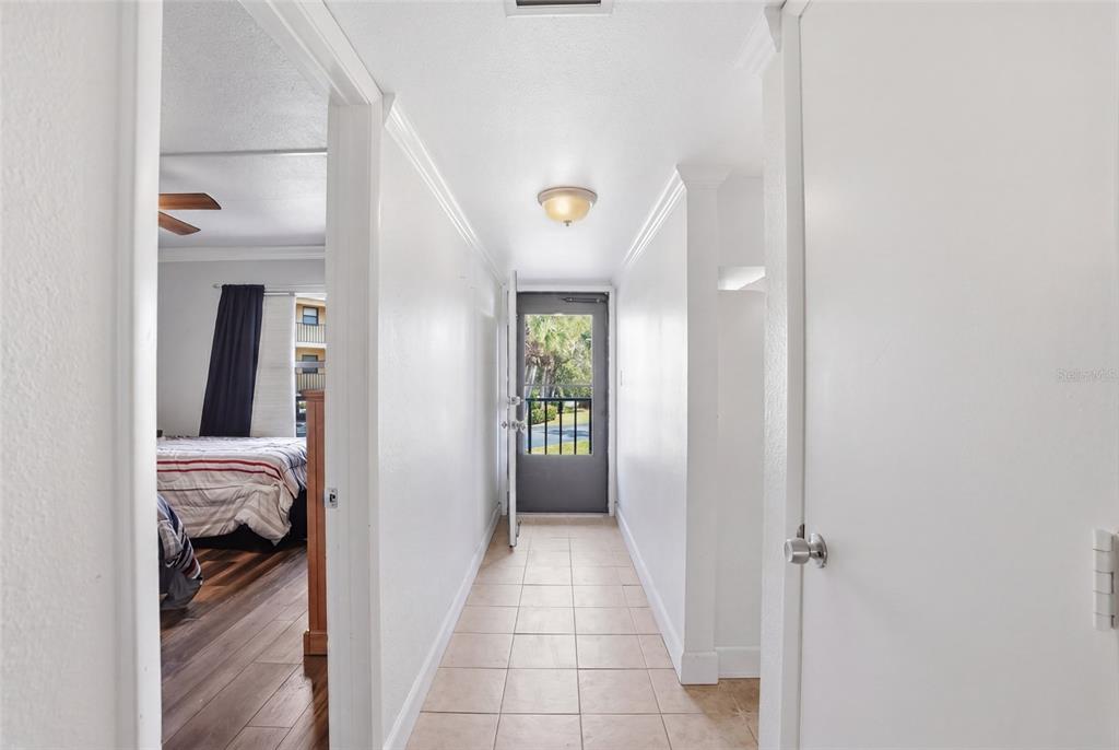 A hallway with tile flooring leads to an exterior door with a view of trees — 14459 RIVER BEACH DRIVE UNIT 115, PORT CHARLOTTE, FL