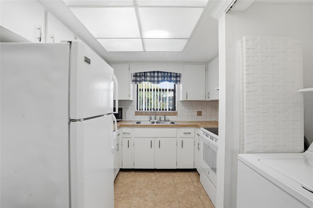 A kitchen with white cabinets, a white refrigerator, a double sink, and tile flooring — 14459 RIVER BEACH DRIVE UNIT 115, PORT CHARLOTTE, FL
