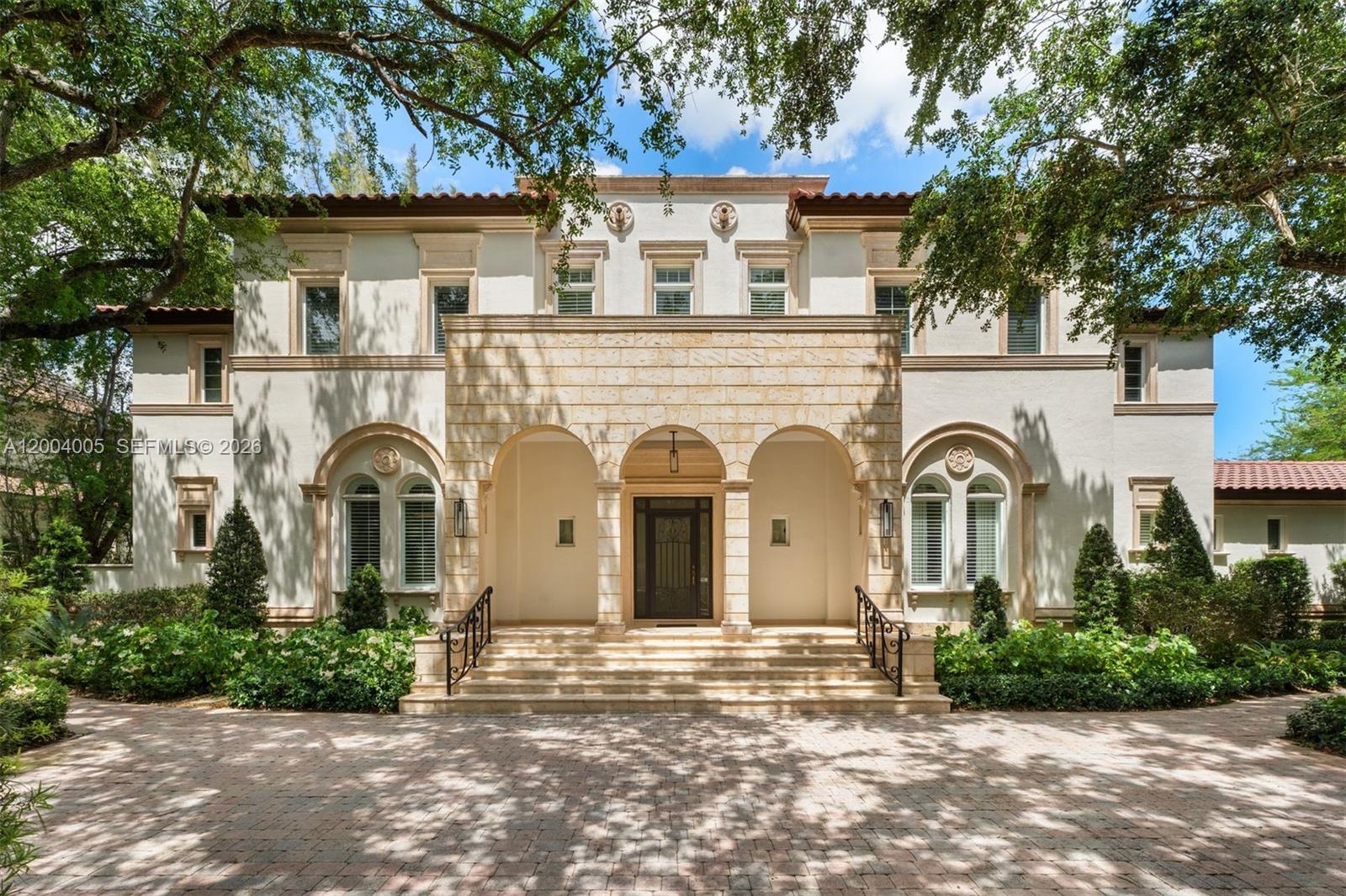 A two-story Mediterranean-style house features a stone-arched entryway, a tiled roof, and a paved driveway — 255 Cocoplum Rd, Coral Gables FL 33143, CORAL GABLES, FL