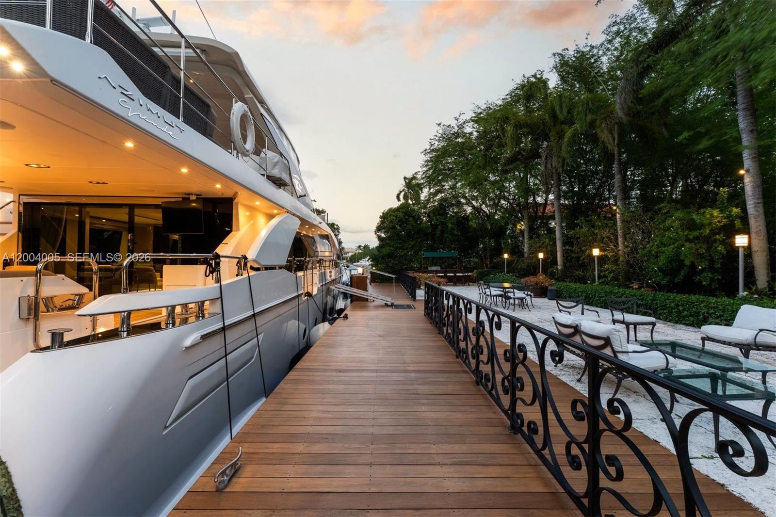 A large yacht is docked alongside a wooden pier with outdoor seating and landscaping — 255 Cocoplum Rd, Coral Gables FL 33143, CORAL GABLES, FL
