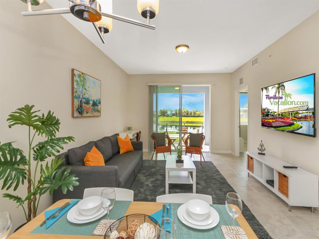 A living room and dining area with a grey sofa, white furniture, and a balcony view — 3151 PARADOX CIRCLE UNIT 104, KISSIMMEE, FL