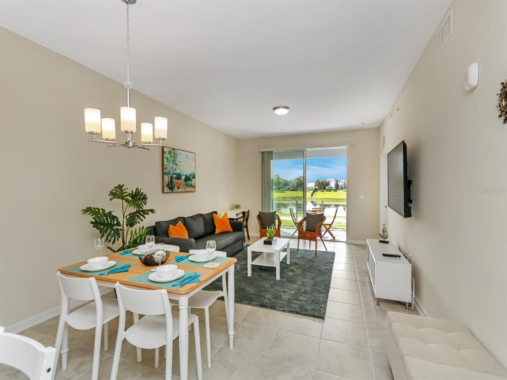 A living and dining room with tile floors, a sliding glass door, and lake views — 3151 PARADOX CIRCLE UNIT 104, KISSIMMEE, FL