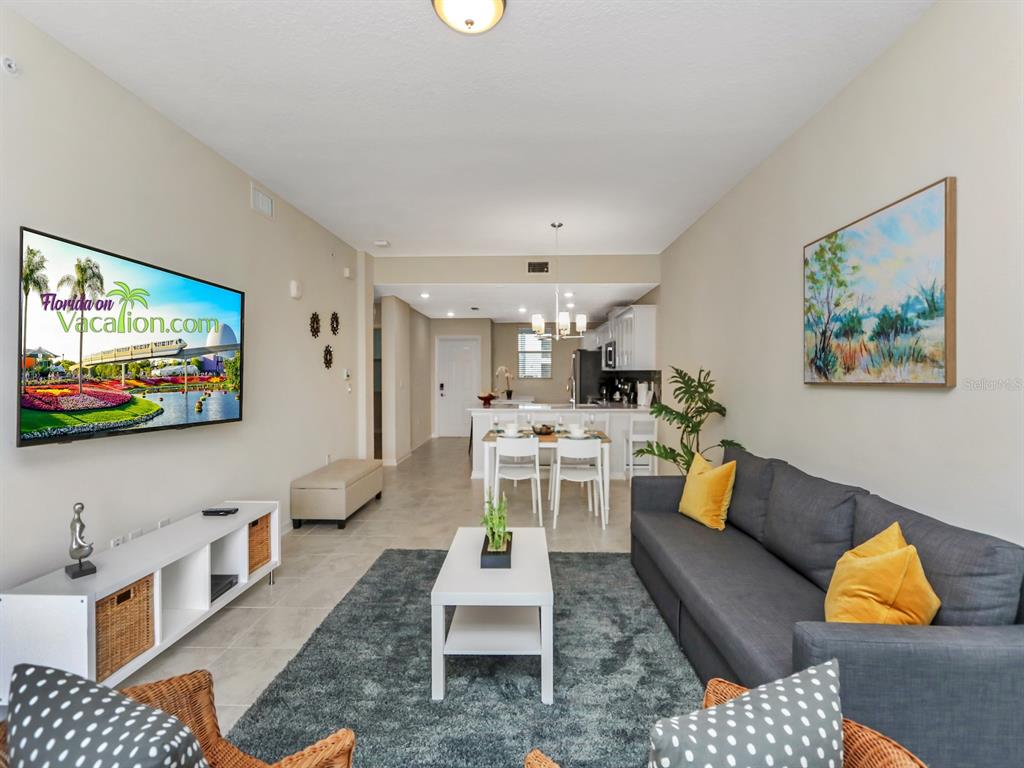 A living room with a gray sofa, white coffee table, and television faces an open kitchen — 3151 PARADOX CIRCLE UNIT 104, KISSIMMEE, FL