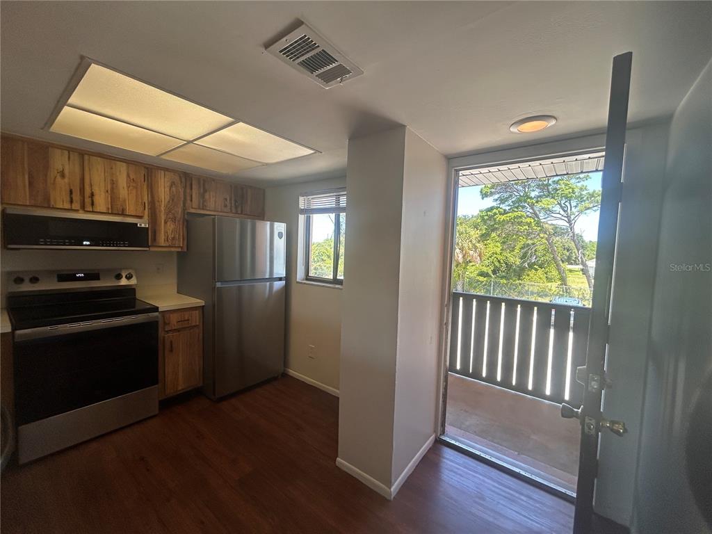 A kitchen with wood cabinets, stainless steel appliances, and a door leading to a balcony — 1712 UNIVERSITY LN UNIT 307, COCOA, FL