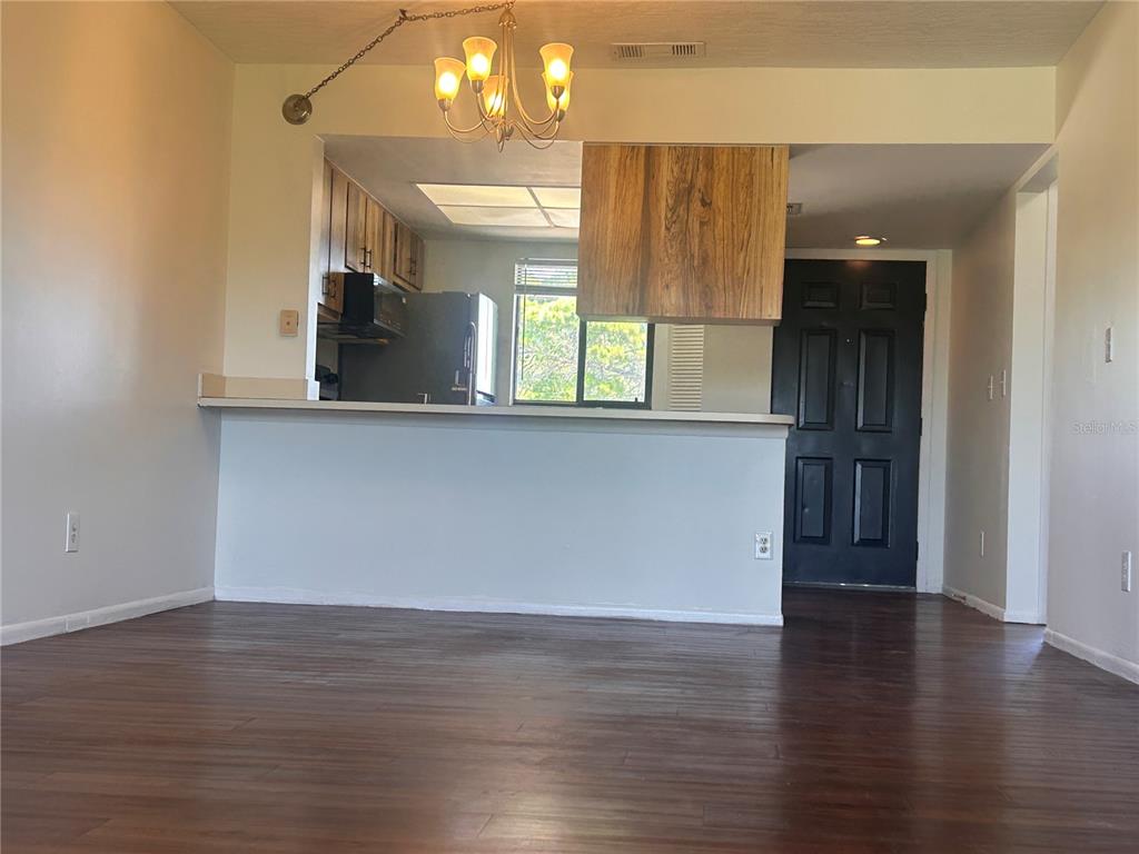 A living area with dark wood flooring looks toward a kitchen with a breakfast bar — 1712 UNIVERSITY LN UNIT 307, COCOA, FL