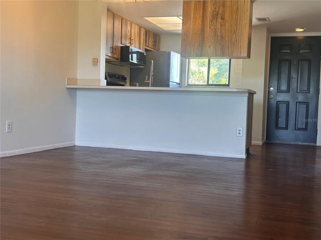 A kitchen with wood cabinets and a breakfast bar overlooks a room with wood flooring — 1712 UNIVERSITY LN UNIT 307, COCOA, FL