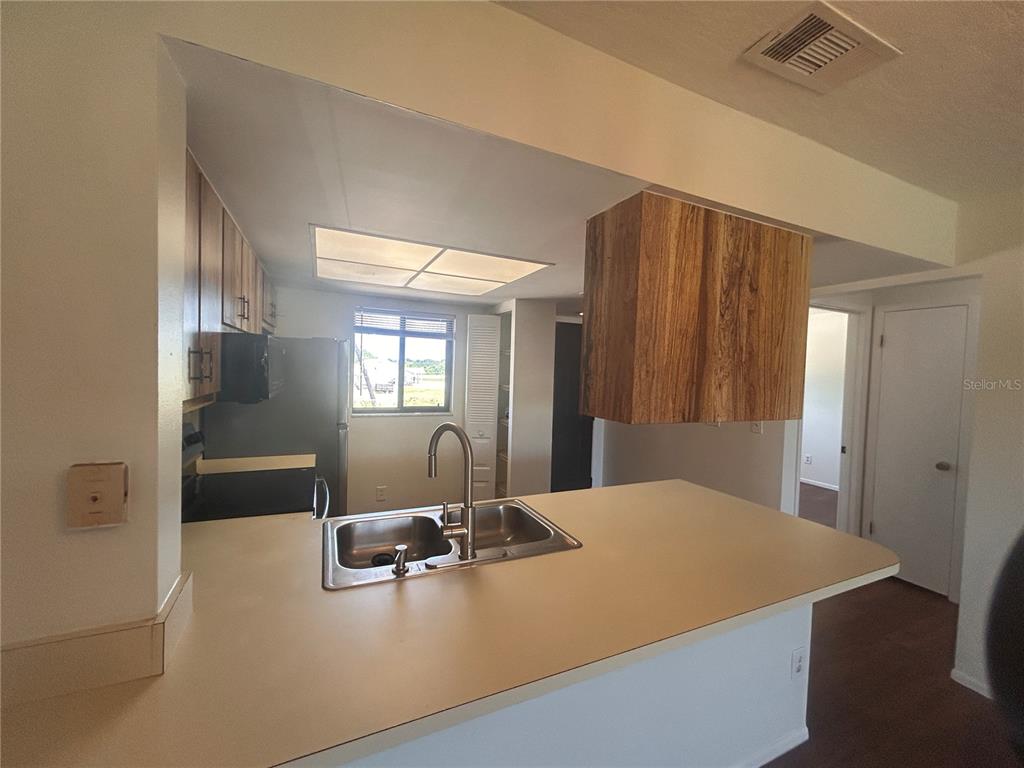 A kitchen features a peninsula with a double sink, wood cabinets, and a drop ceiling — 1712 UNIVERSITY LN UNIT 307, COCOA, FL