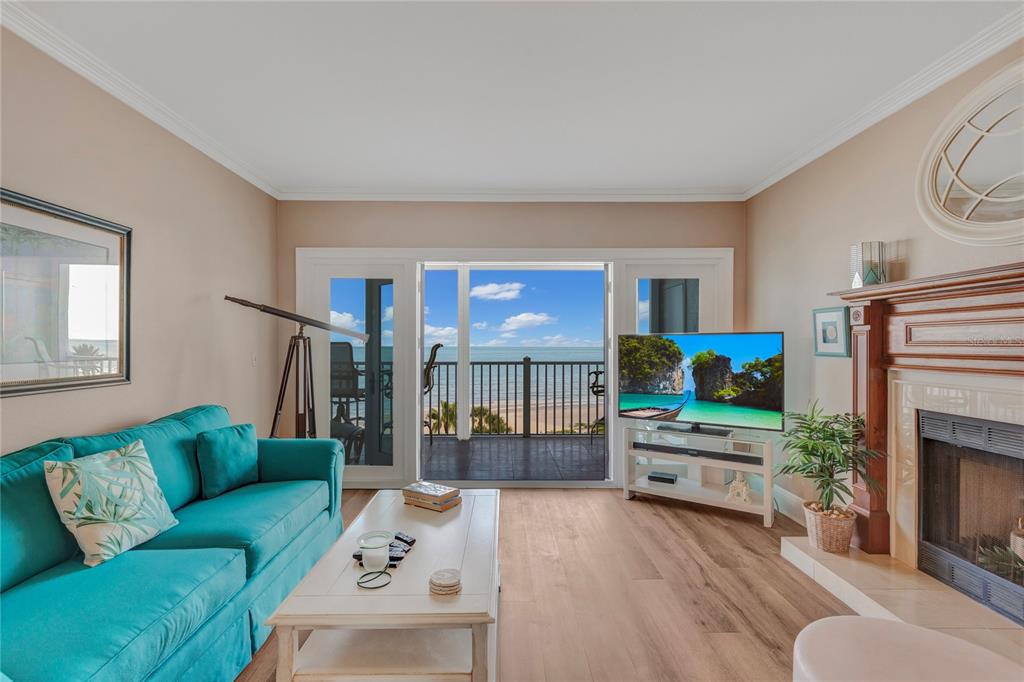 A living room with a teal sofa, fireplace, and sliding doors opening to a beach view — 1582 GULF BOULEVARD UNIT 1506, CLEARWATER BEACH, FL