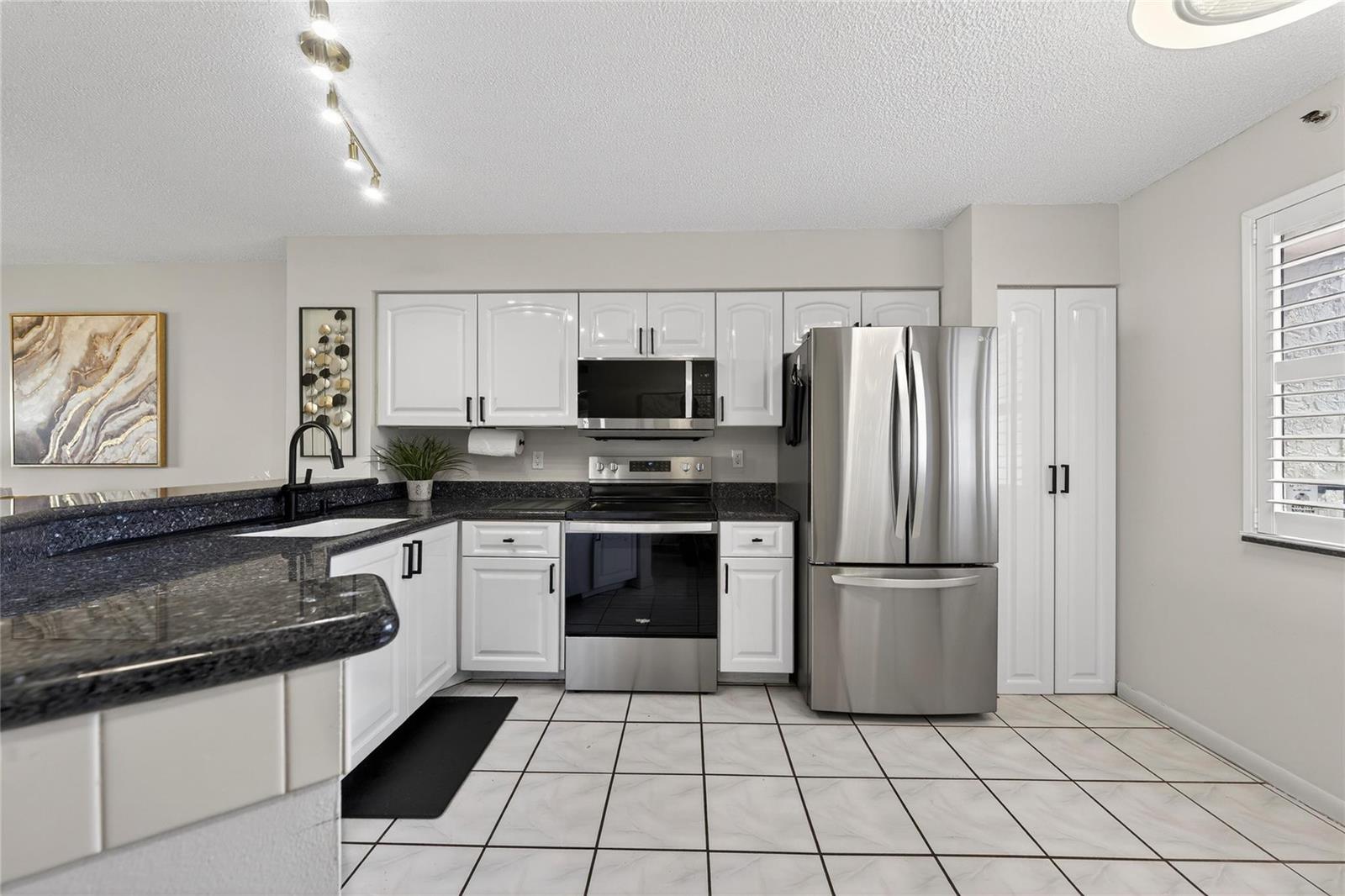 A kitchen features white cabinets, stainless steel appliances, dark granite countertops, and white tile flooring — 2215 Cypress Island Drive # 701, Pompano Beach FL 33069, POMPANO BEACH, FL