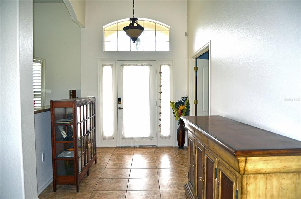 A bright entryway features tiled floors, a wooden cabinet, a display case, and a front door — 4 PINEHURST PLACE, ROTONDA WEST, FL