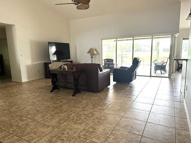 A living room features tile flooring, a brown sofa, a television, and large sliding glass doors — 4 PINEHURST PLACE, ROTONDA WEST, FL