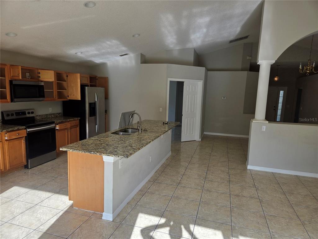 A kitchen with light wood cabinets, granite countertops, a center island, and tile flooring — 725 ROBIN COURT, KISSIMMEE, FL