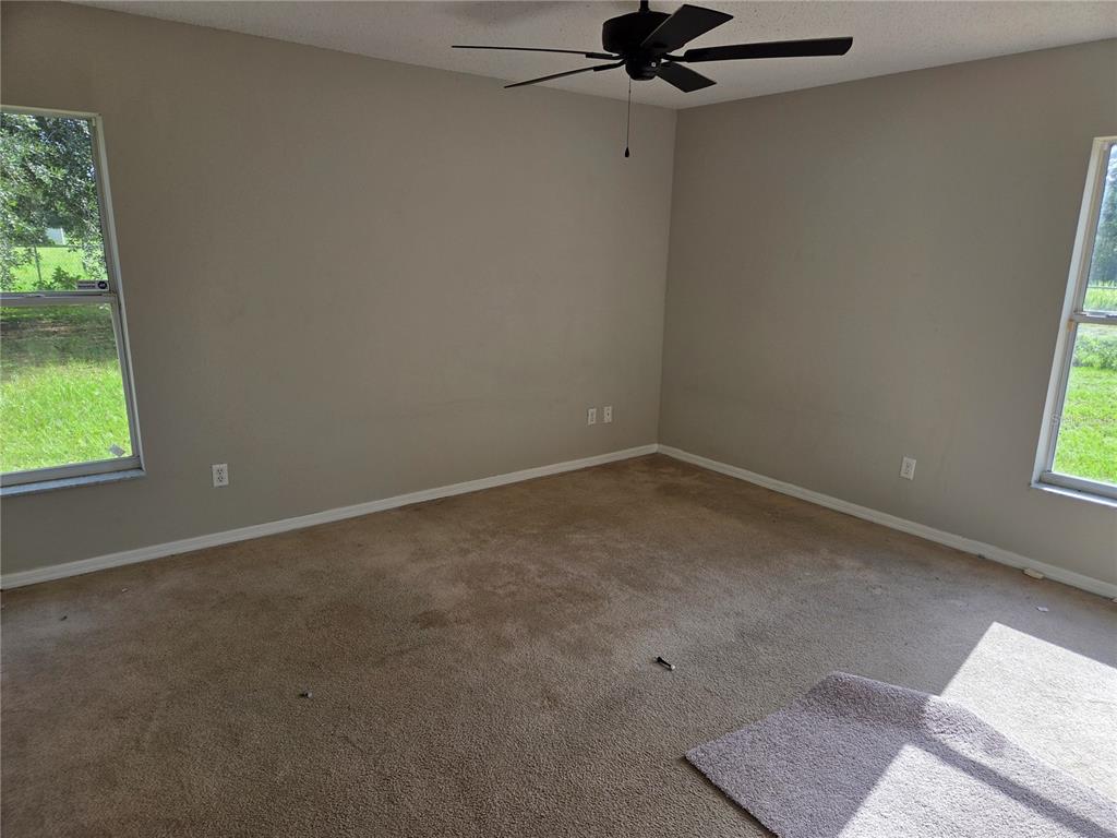 An empty bedroom features beige carpet, light gray walls, a ceiling fan, and two windows — 725 ROBIN COURT, KISSIMMEE, FL
