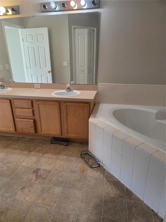 A bathroom features a double vanity with wood cabinets, a large mirror, and a tiled tub — 725 ROBIN COURT, KISSIMMEE, FL