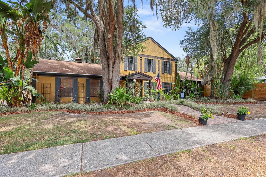 A two-story yellow house with dark shutters sits behind large trees and a sidewalk — 314 BLOOMINGFIELD DRIVE, BRANDON, FL