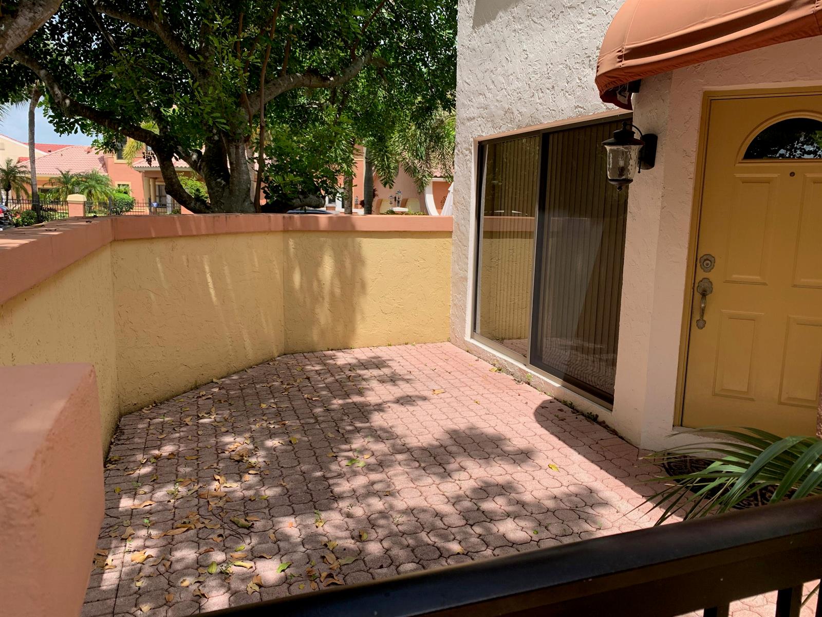 A paved patio area sits beside a yellow door and a sliding glass door — 49 Uno Lago Drive, Juno Beach FL 33408, JUNO BEACH, FL