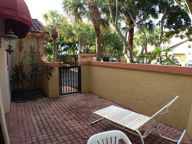 A paved patio features a lounge chair, a small gate, and surrounding tropical landscaping — 49 Uno Lago Drive, Juno Beach FL 33408, JUNO BEACH, FL