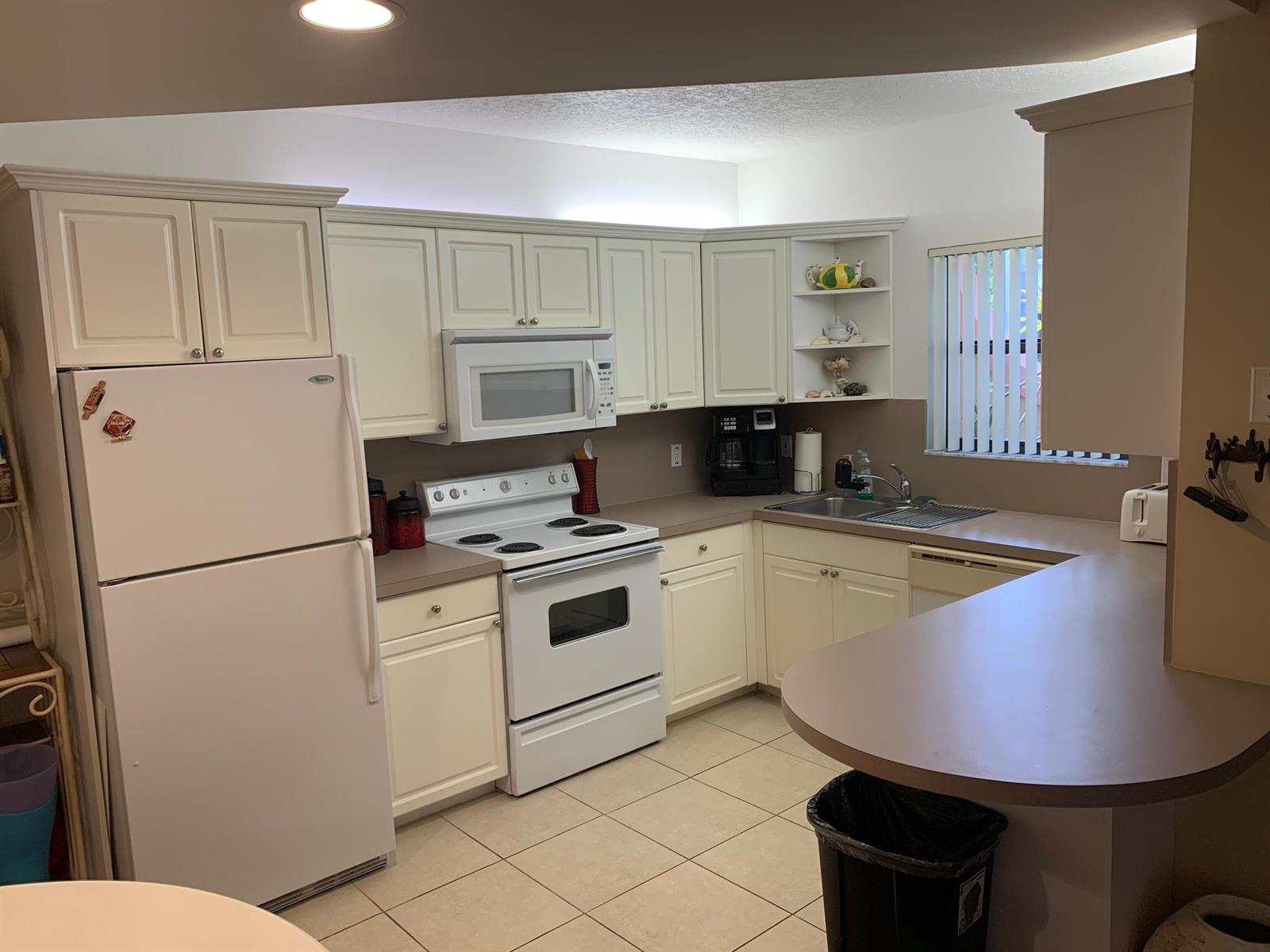 A kitchen with white cabinets, white appliances, a beige countertop, and light-colored tile flooring — 49 Uno Lago Drive, Juno Beach FL 33408, JUNO BEACH, FL