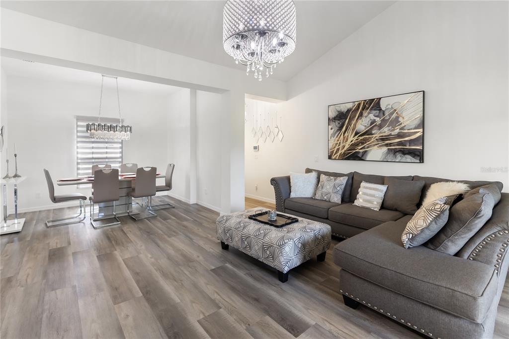 A living room and dining area feature gray wood-look flooring and modern crystal chandeliers — 3271 JERSEY STREET, PORT CHARLOTTE, FL