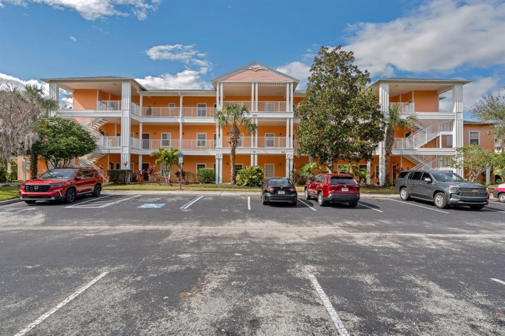 A three-story orange apartment building with white balconies and a parking lot in front — 301 NEW PROVIDENCE PROMENADE UNIT 301, DAVENPORT, FL