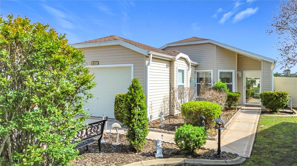 A tan-sided house features a concrete walkway leading to a glass-paned front door — 4844 HERON RUN CIRCLE, LEESBURG, FL