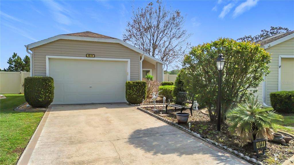 A single-story house with a beige garage, a concrete driveway, and a small landscaped yard — 4844 HERON RUN CIRCLE, LEESBURG, FL