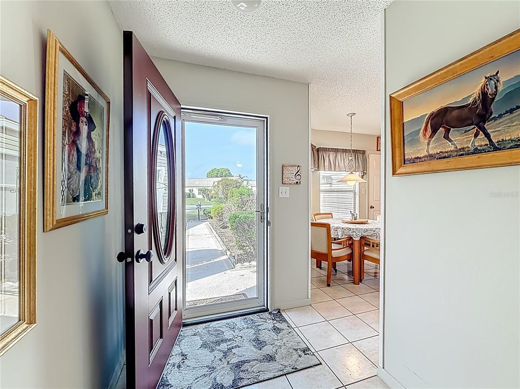 An entryway with a red door, tiled floors, and framed artwork leads to a dining area — 4844 HERON RUN CIRCLE, LEESBURG, FL