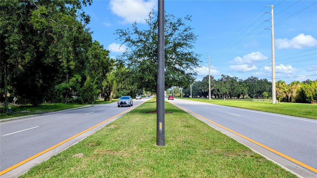 A paved road with a grassy median and a utility pole under a blue sky — 5211 WARM SPRINGS AVENUE, WILDWOOD, FL