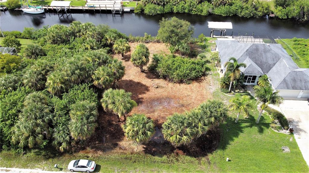 An aerial view shows a vacant lot with palm trees next to a residential house — 18037 OHARA DRIVE, PORT CHARLOTTE, FL